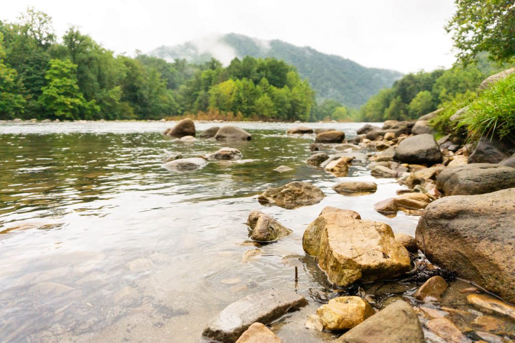 rocks along a riverbank with mountains in the background