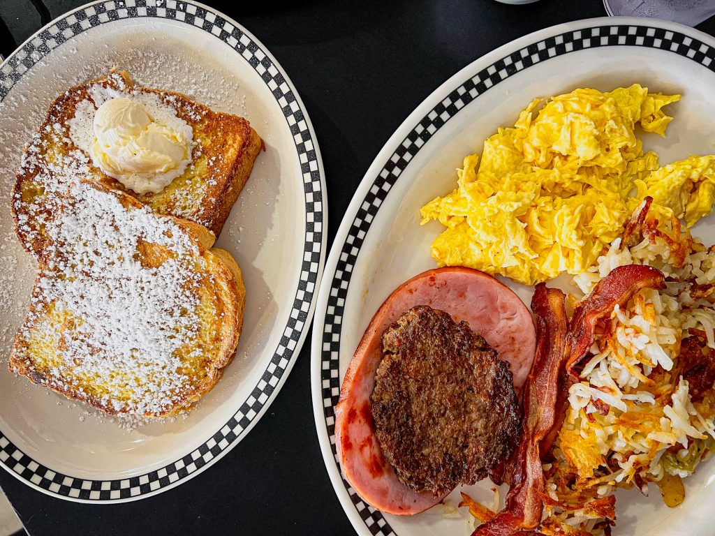 french toast on one plate and ham, sausage, bacon, eggs, and hashbrowns on another