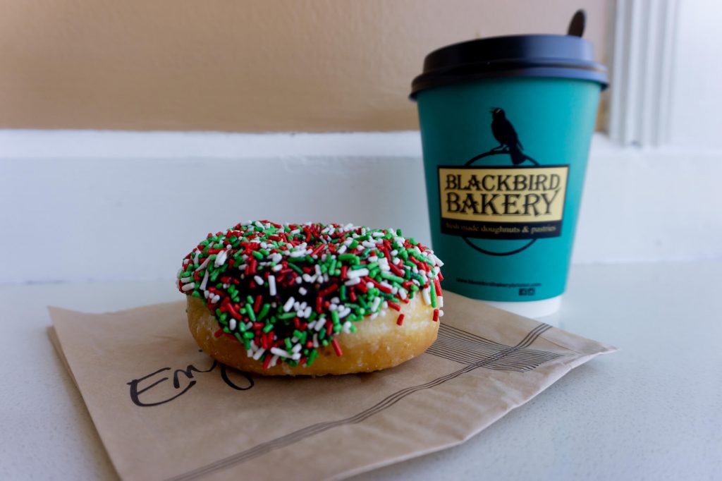 Donut with multi-colored sprinkles on top beside a to-go coffee cup.