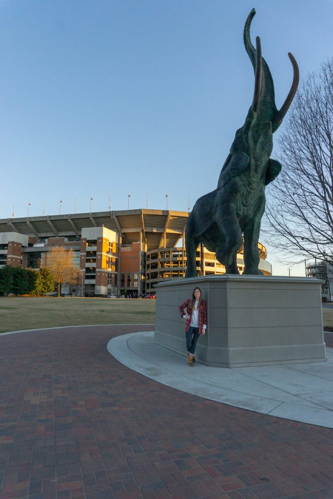 girl standing by elephant statue in front of giant football stadium