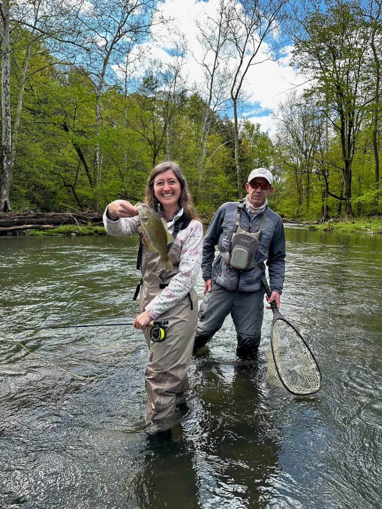 Girl holding fish with guide behind her. Fly fishing is one of the best things to do near Lewistown, PA.