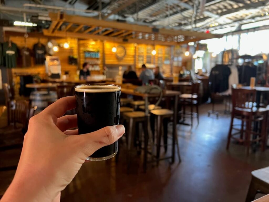 Hand holding a sample of beer in front of tasting room for the brewery walking tour in Asheville.