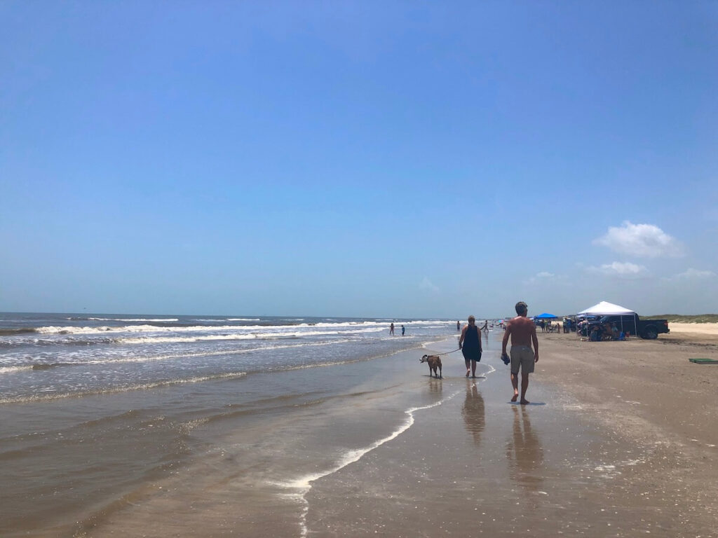 People walking down the beach to where there are cars parked and tents set up.