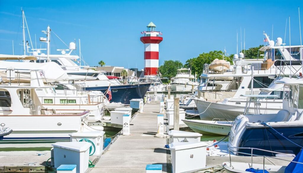 Red and white striped lighthouse at the end of a marina full of boats.