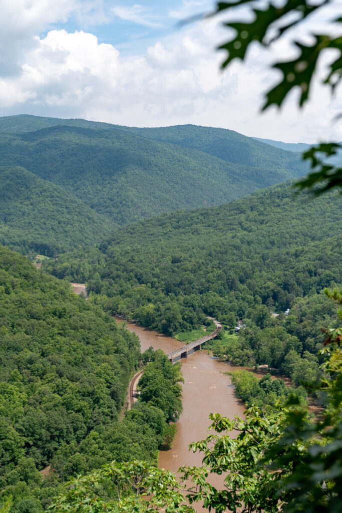 Muddy Nolichucky River down below with a train trestle crossing it and mountains in the background.