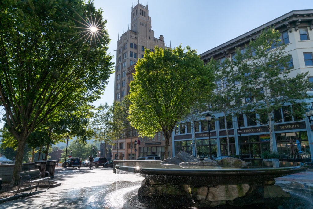 Small park in Asheville with a fountain and beautiful buildings in the background.