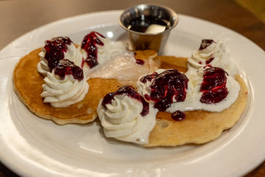 Plate of pancakes with whipped cream and berry compote.