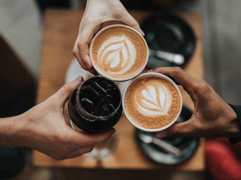 Two people holding lattes and one holding a cold brew seen from above.