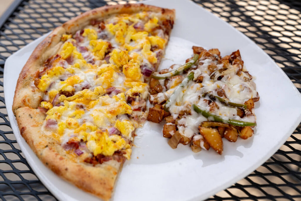 Pizza with eggs, bacon, ham, and cheese as toppings and side of potatoes with cheese.