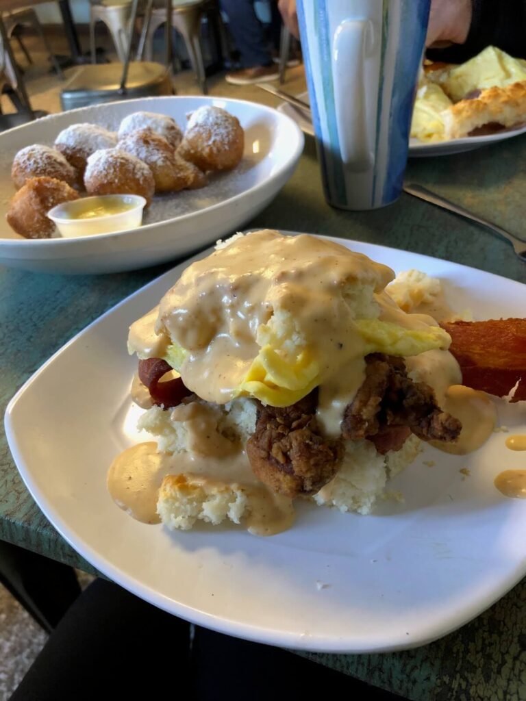 Biscuit with chicken, eggs, and bacon smothered in gravy with biscuit donuts in the background.