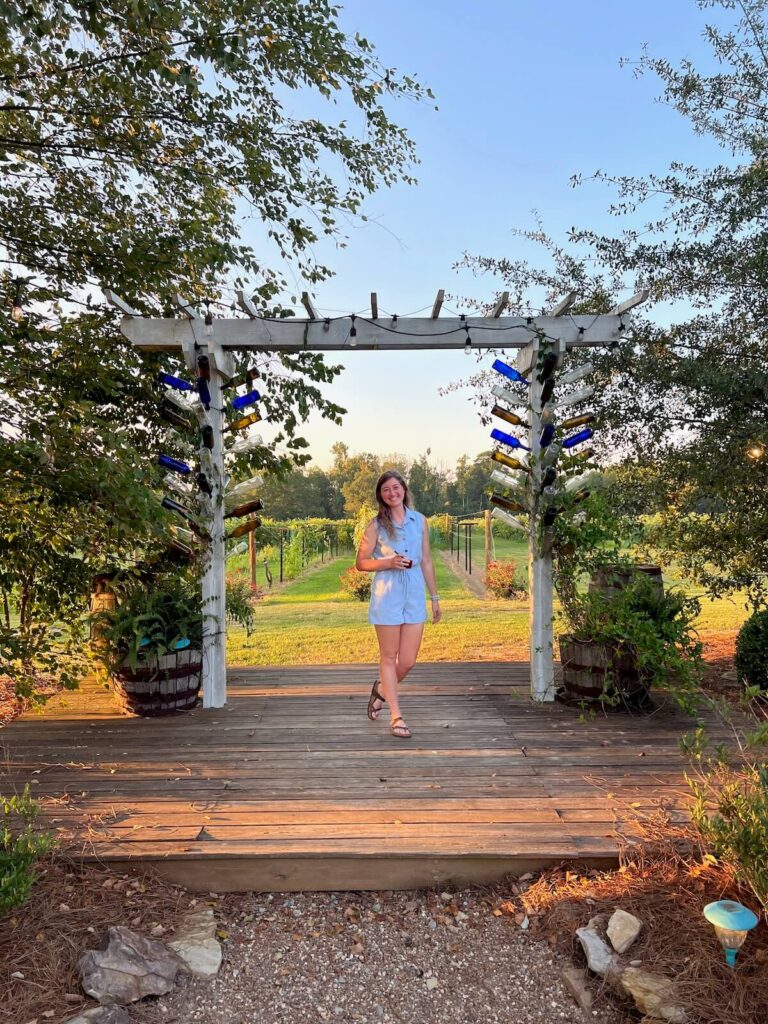 Girl in front of pergola frame with wine bottles enjoying the things to do in Guntersville, AL.