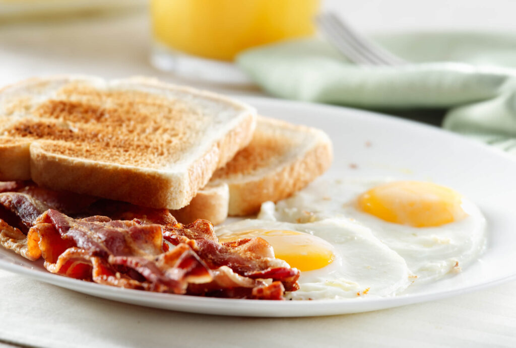 Sunny side up eggs, bacon, and toast on a white plate.