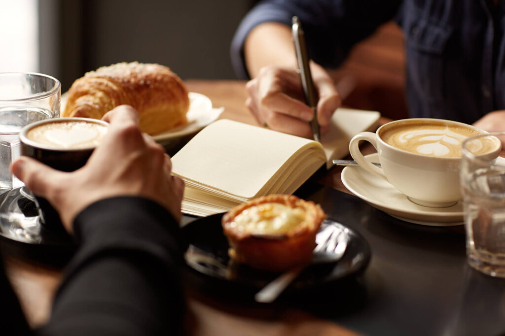 Pastries and coffee on the counter with person writing in a notebook.