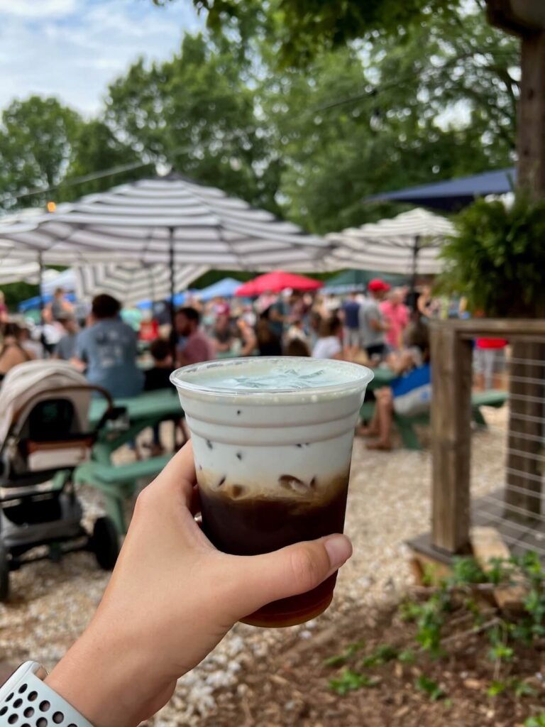 Hand holding iced coffee with blue cold foam on top.