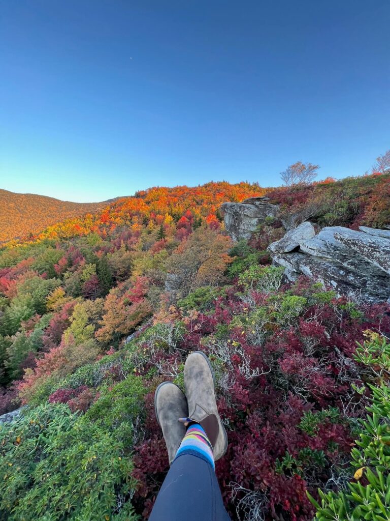 two feet hanging over ledge with fall colors along the mountain in the background