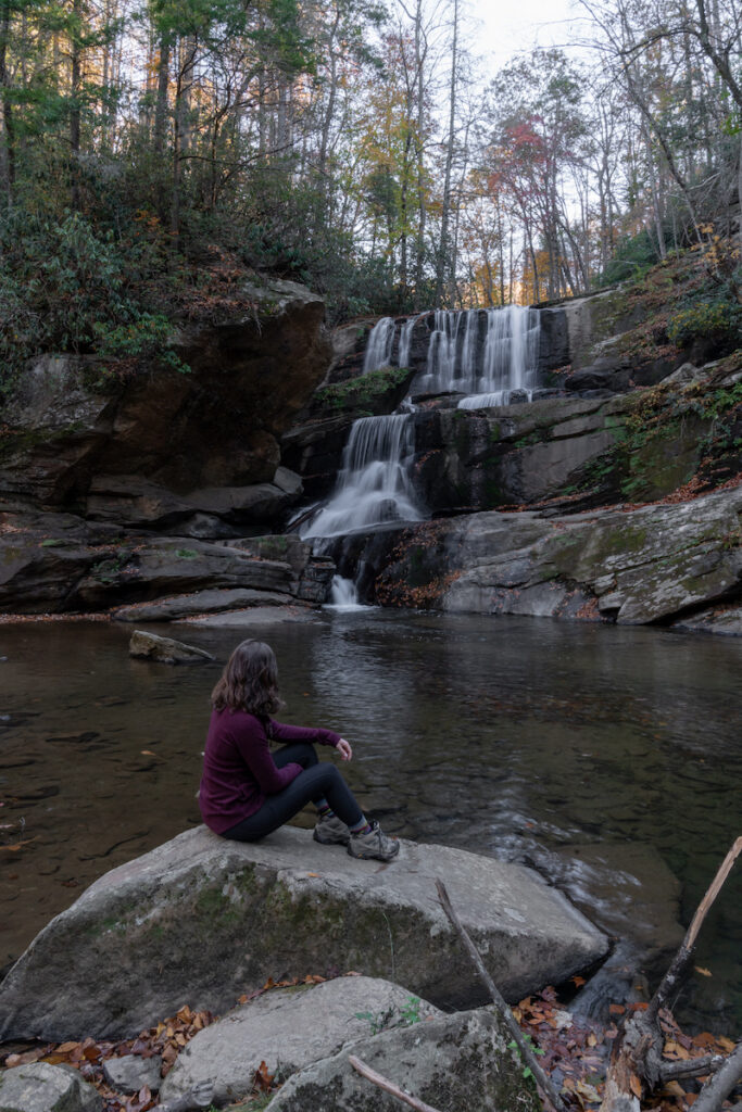 Girl sitting on rock in front of waterfall.