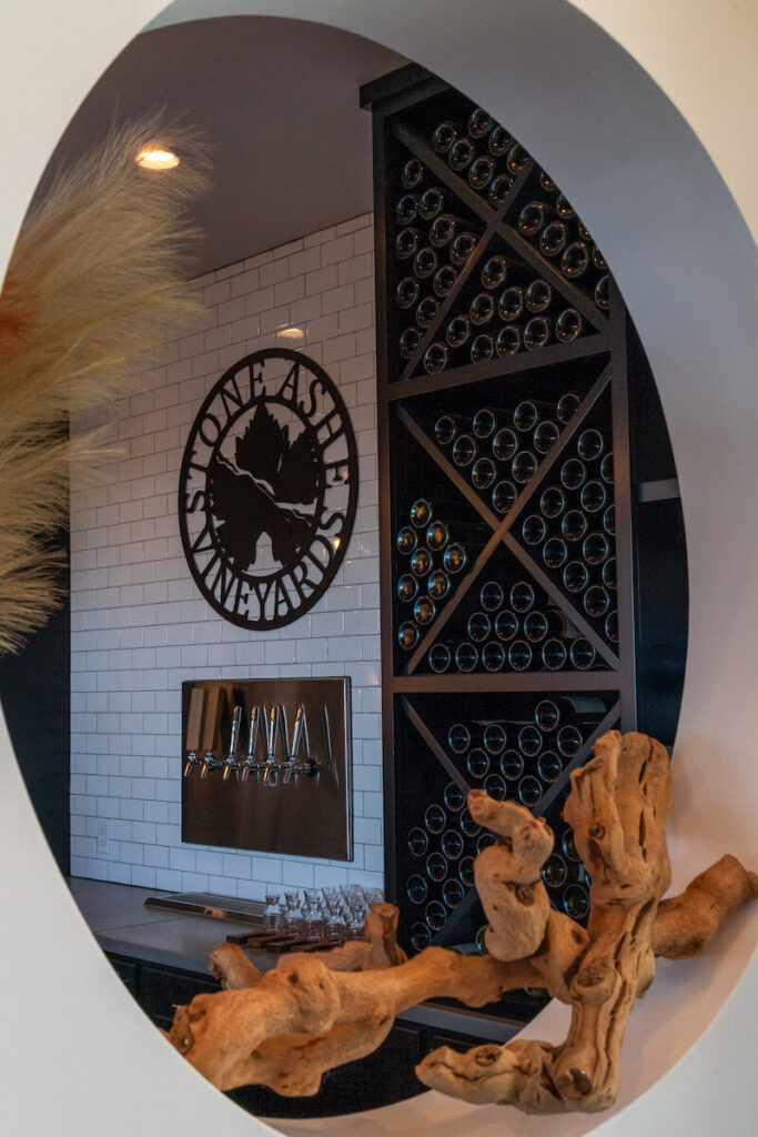 Stone Ashe Vineyards logo above wine taps in between stacked wine bottles behind the bar