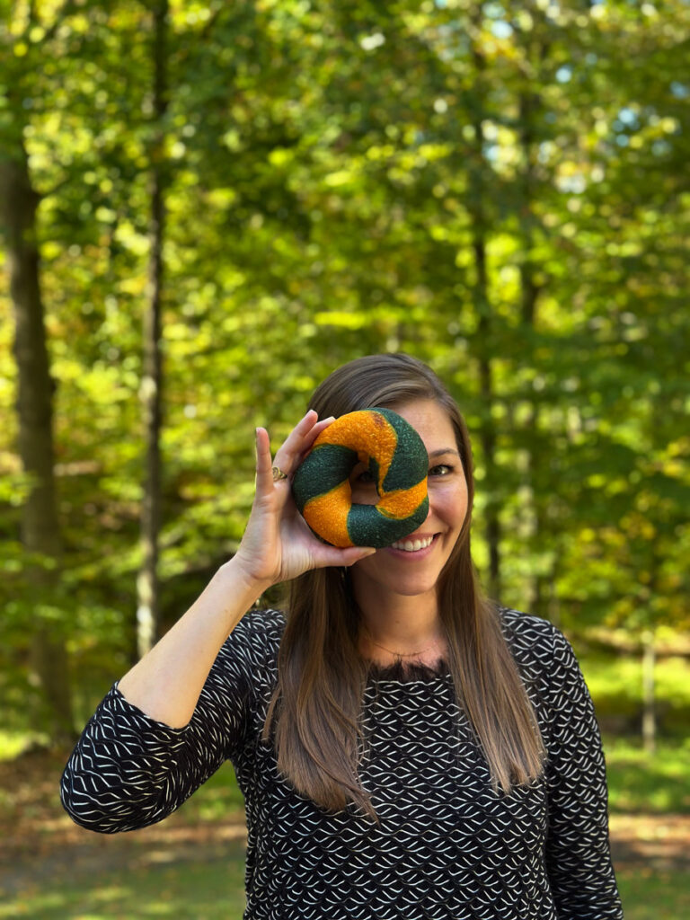 girl holding a green and gold bagel and looking through the center hole