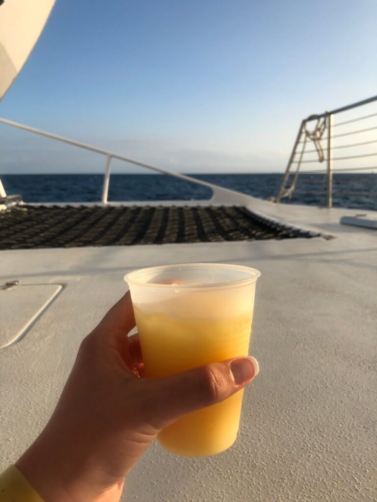 girl holding a painkiller cocktail in front of an ocean view from a boat
