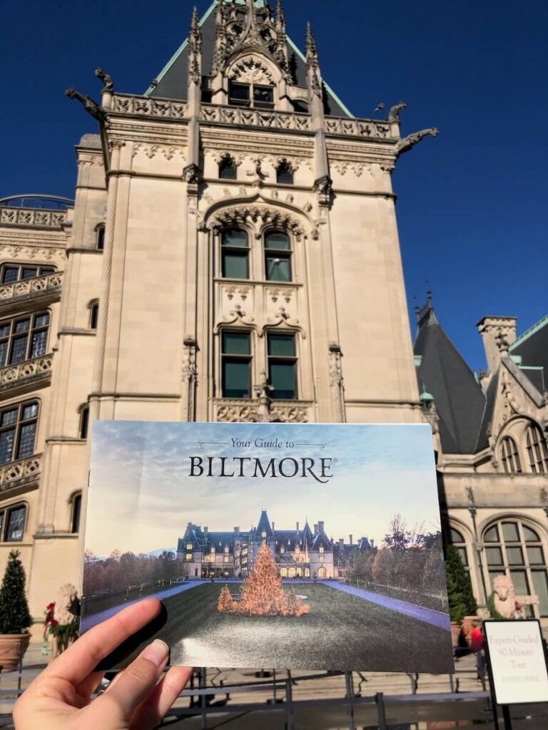 Woman holding up a guide to visiting Biltmore in front of the house.