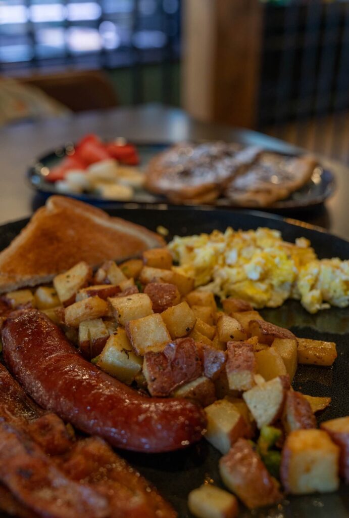 breakfast plate with eggs, potatoes, sausage, bacon, and toast