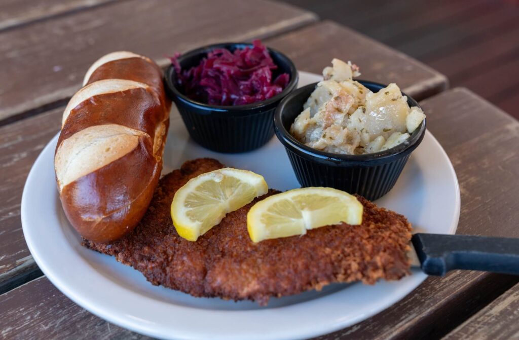plate of schnitzel, potato salad, red cabbage, and pretzel roll