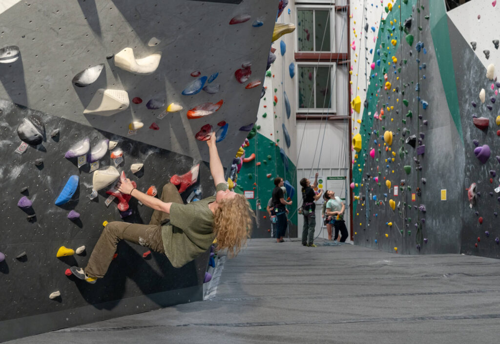 man climbing up a boulder wall in a climbing gym