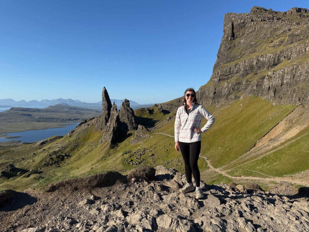 woman standing in front of viewpoint on Old Man of Storr hike with mountains and ocean in the background