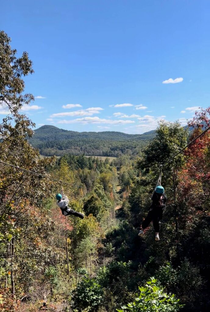 two girls on dual zipline with views of the mountains in background