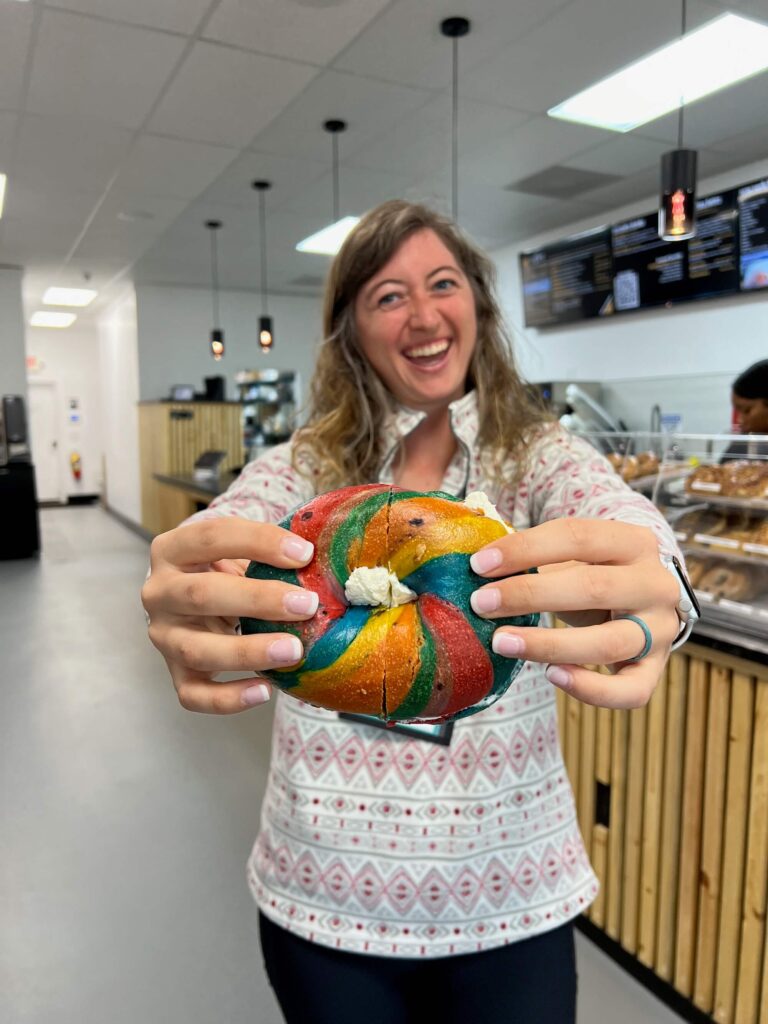 girl holding a rainbow bagel with cream cheese