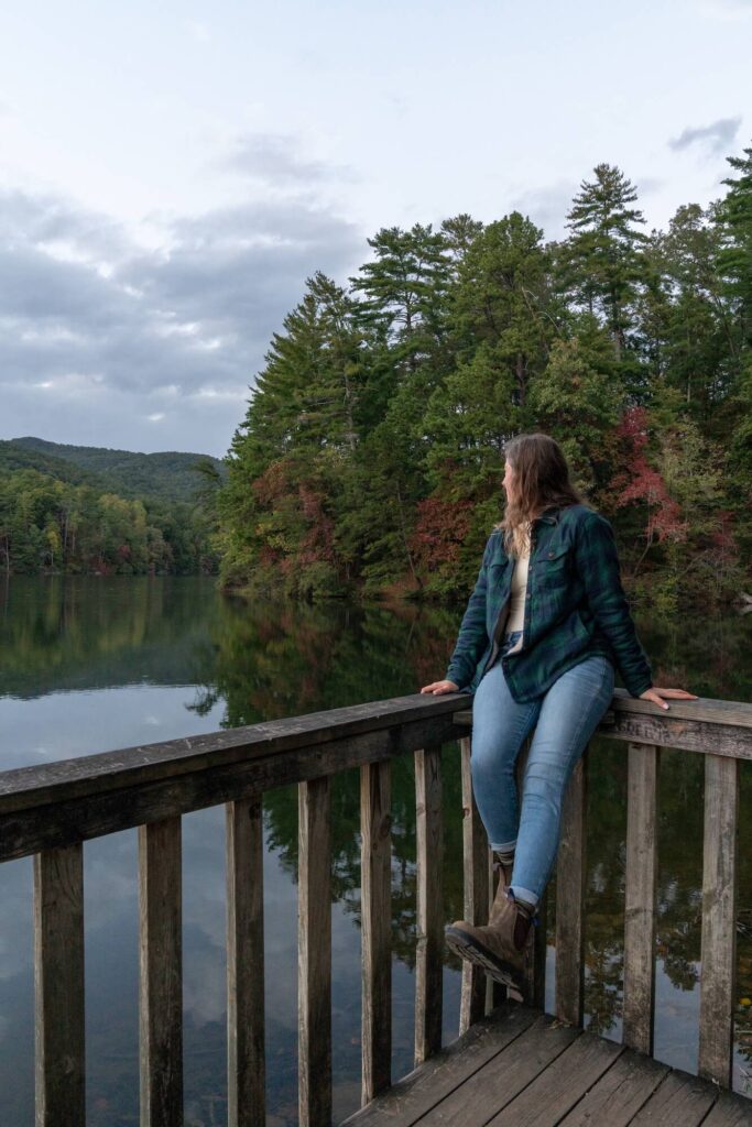 A girl sitting on the deck railing looking out over a lake as the trees begin to change colors in fall.