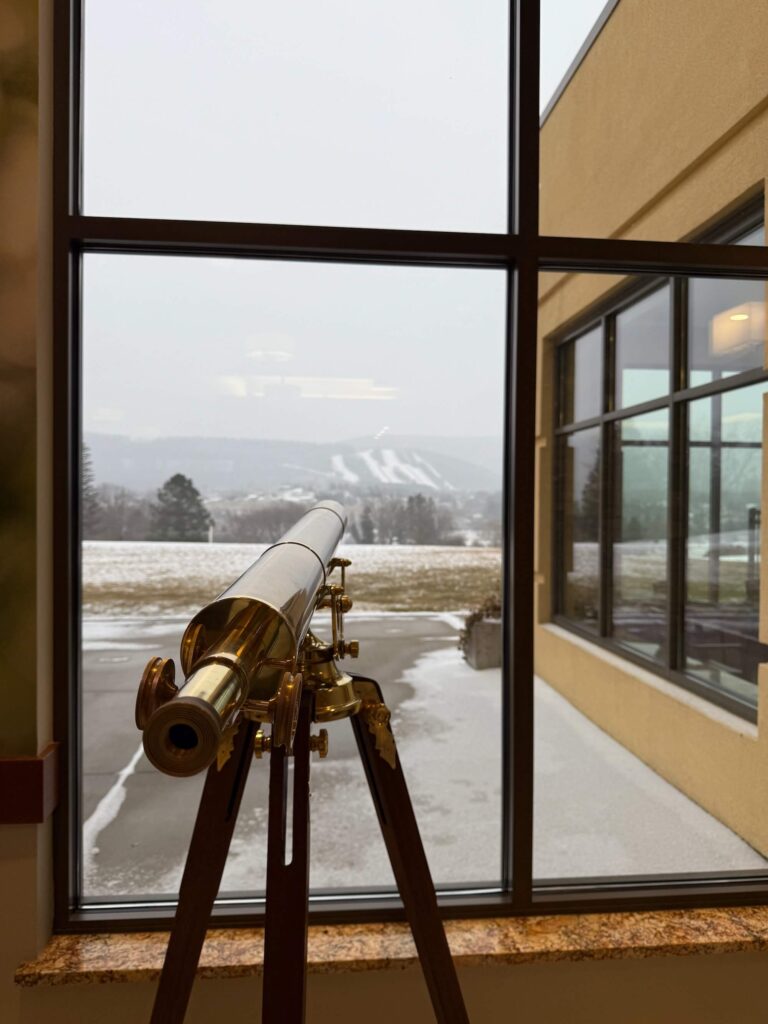 telescope in front of a window where you can see a ski mountain in the distance