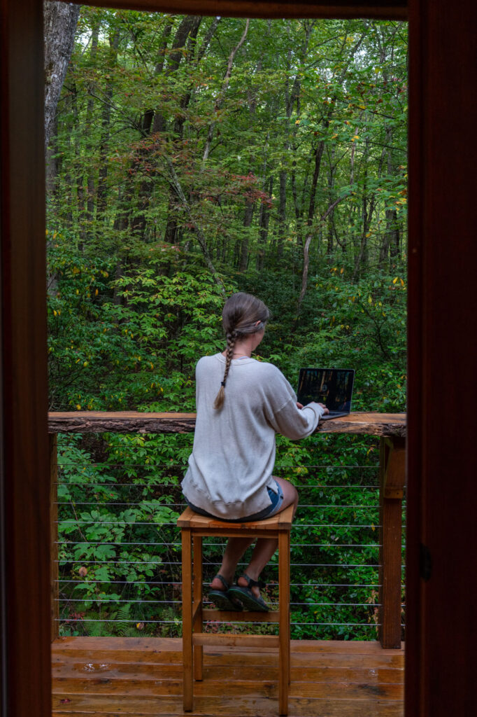 A girl sitting on an outdoor deck working on her laptop. My laptop is one of the most important pieces of gear I use as a travel content creator.