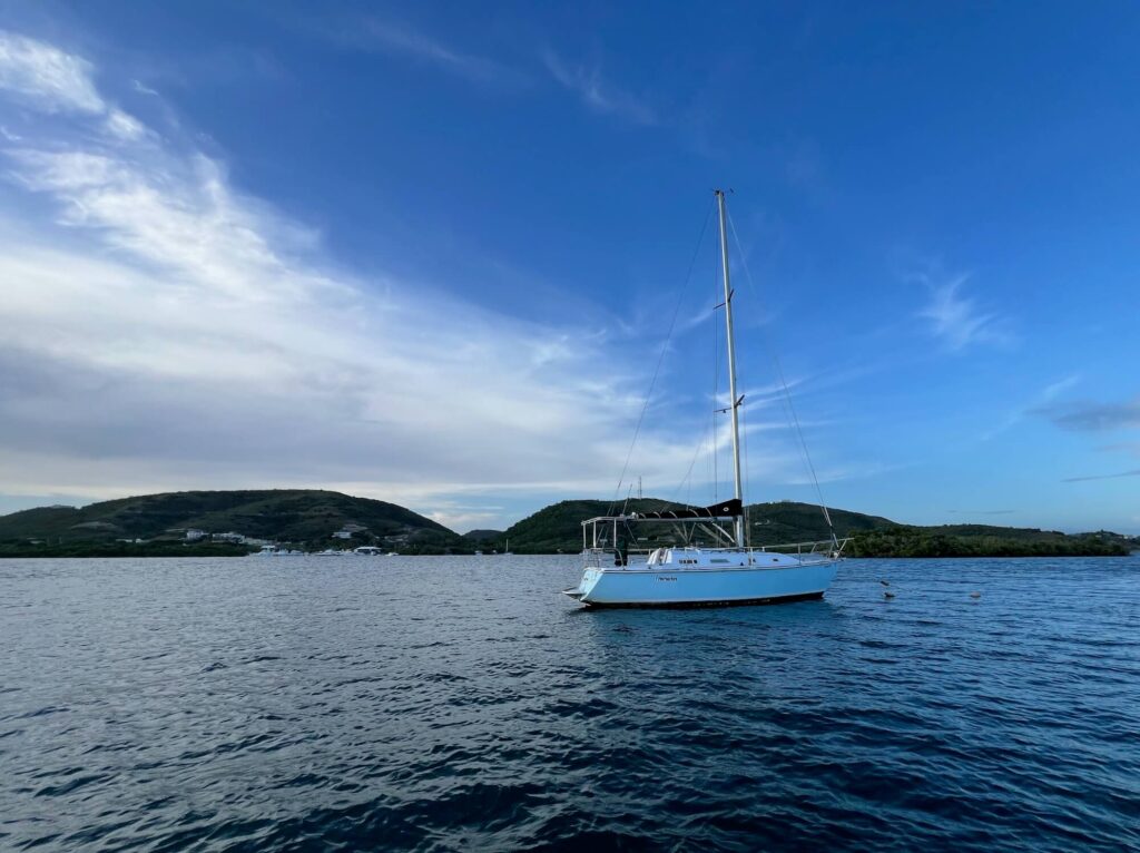 Sailboat anchored offshore with the shoreline and mountains in the background.