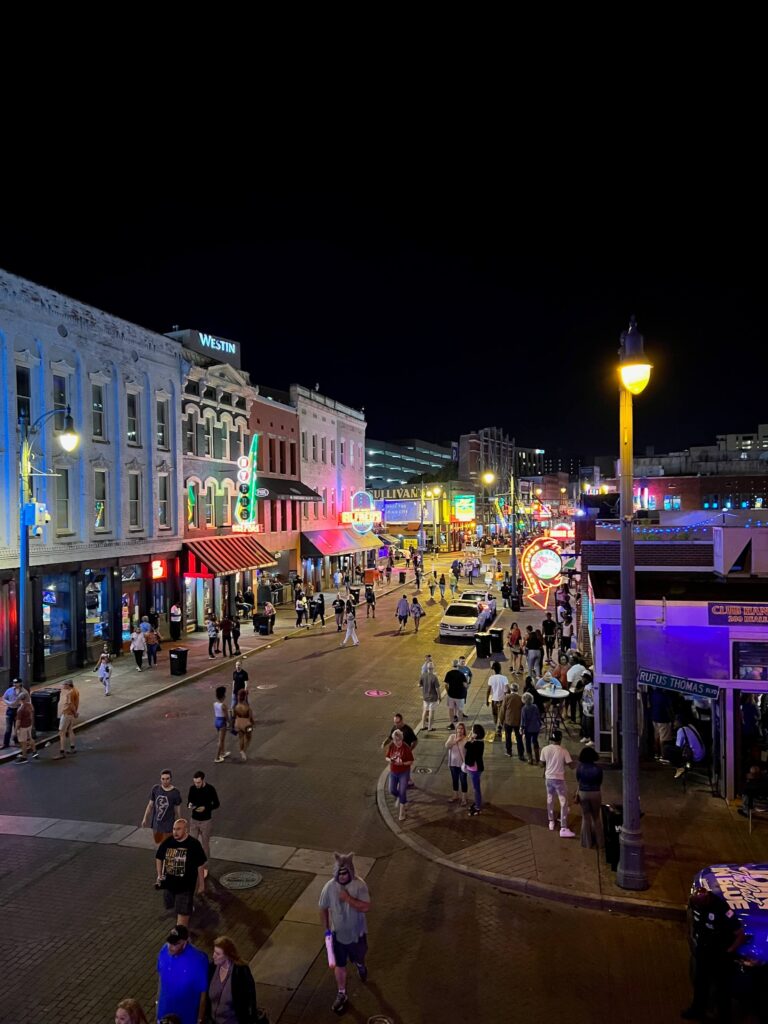 View of Memphis streets lit up in the evening with crowds walking on the sidewalks and roads. Memphis was home to one of the recent TravelCon travel blogging conferences.